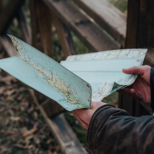 Close-up of hands holding a map outdoors by a wooden fence in autumn.